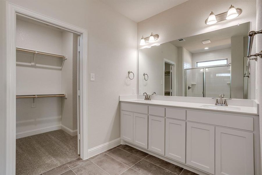 Bathroom with a spacious closet, double vanity, a stall shower, and light tile patterned floors