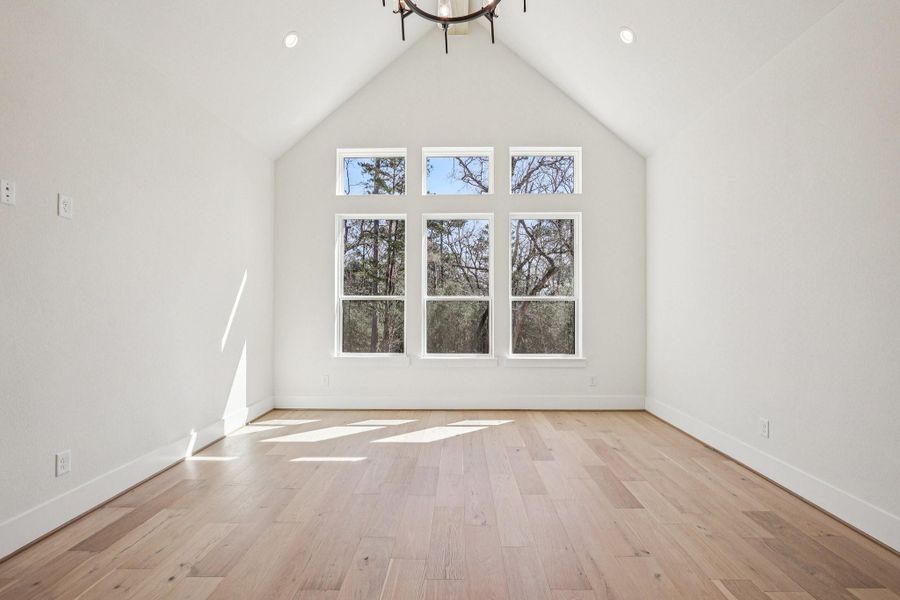 Bright and spacious primary bedroom with high ceilings and large windows offering scenic views. It features light wood flooring and a modern chandelier, perfect for a serene living space.