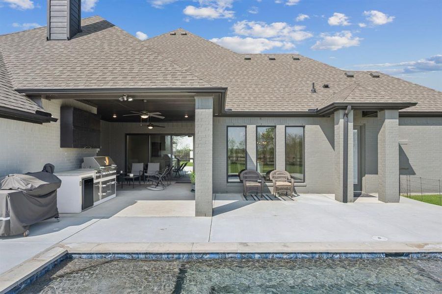 Back of house with a shingled roof, area for grilling, a patio area, an outdoor pool, and brick siding