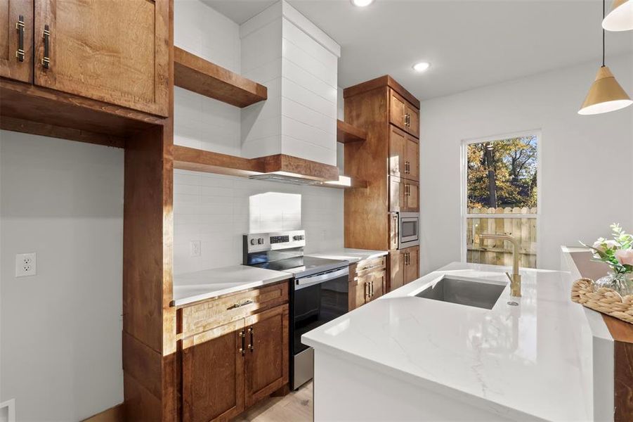 Kitchen featuring sink, tasteful backsplash, light stone counters, decorative light fixtures, and appliances with stainless steel finishes