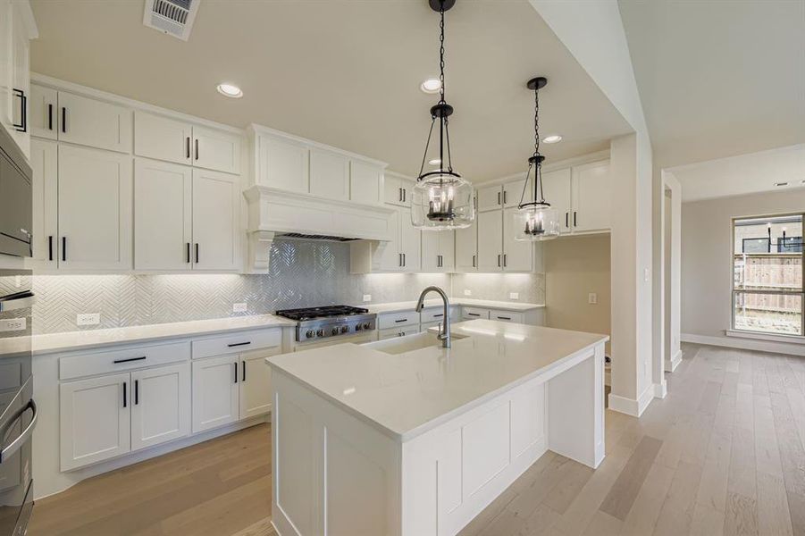 Kitchen featuring tasteful backsplash, light wood finished floors, a kitchen island with sink, recessed lighting, and decorative light fixtures