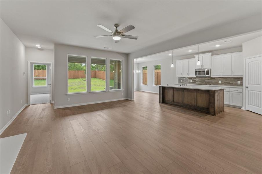 Spacious open-concept living area featuring wood-finish flooring, a ceiling fan, and large windows overlooking the backyard