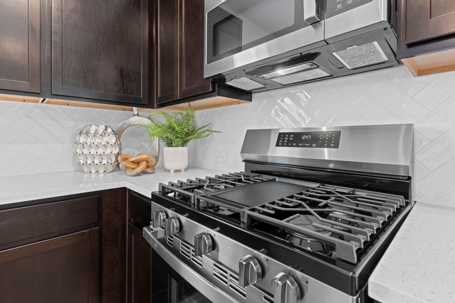 Close-up of the freestanding gas range with five Burners, built-in microwave, and Glass subway tile backsplash showcases the kitchen’s high-end finishes and modern stainless-steel appliances—perfect for cooking enthusiasts. **Image Representative of Plan Only and May Vary as Built**. Close-up of the freestanding gas range with five Burners, built-in microwave, and Glass subway tile backsplash showcases the kitchen’s high-end finishes and modern stainless-steel appliances—perfect for cooking enthusiasts. **Image Representative of Plan Only and May Vary as Built**.