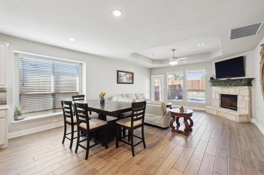 Dining area with a fireplace, a tray ceiling, light hardwood / wood-style flooring, and ceiling fan