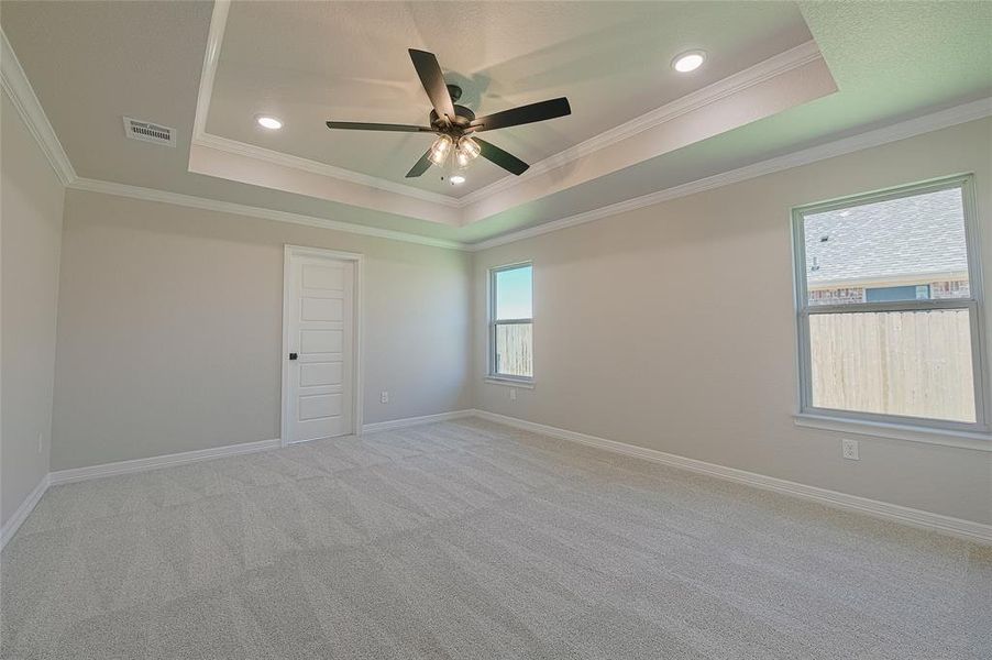 Empty room with a raised ceiling, crown molding, light colored carpet, recessed lighting, and ceiling fan