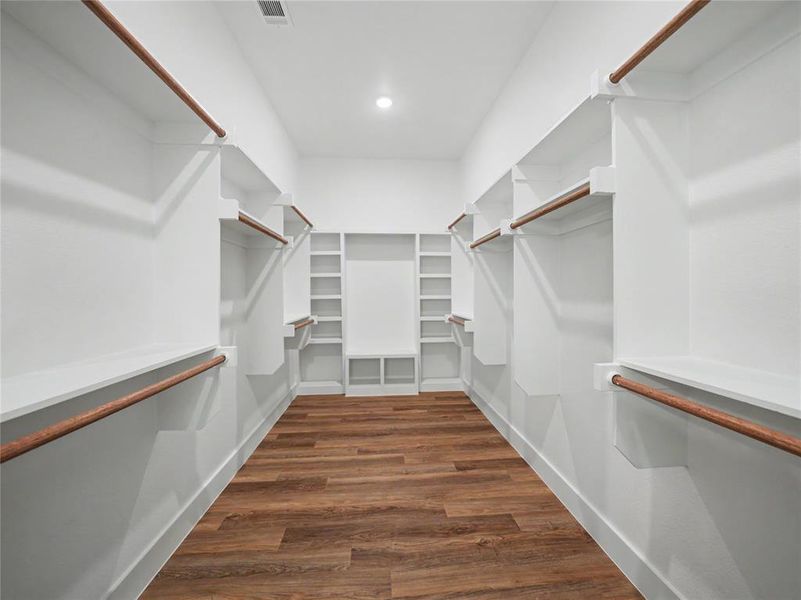 Spacious walk-in closet featuring wood-finish flooring, extensive built-in shelving, multiple hanging rods, and recessed lighting