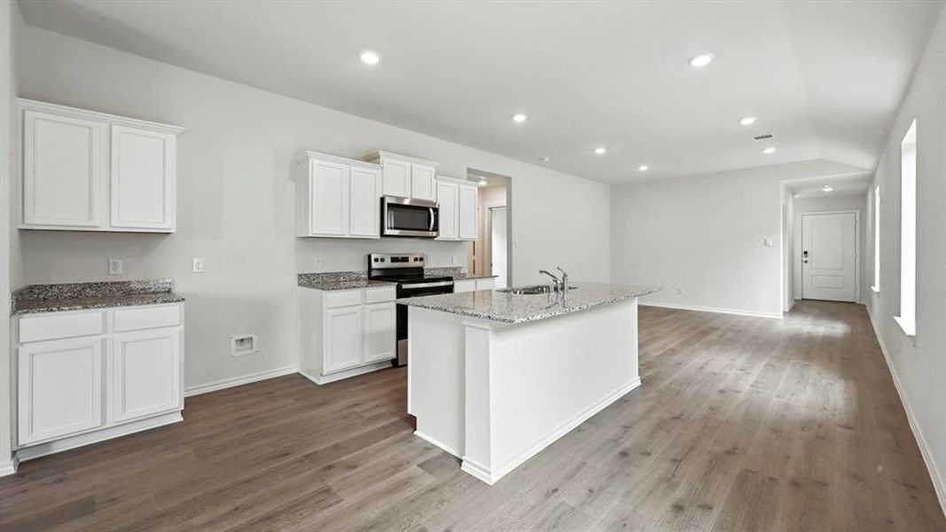 Open-concept kitchen featuring an island with a double sink, white cabinetry, granite countertops, and stainless steel appliances Open-concept kitchen featuring an island with a double sink, white cabinetry, granite countertops, and stainless steel appliances