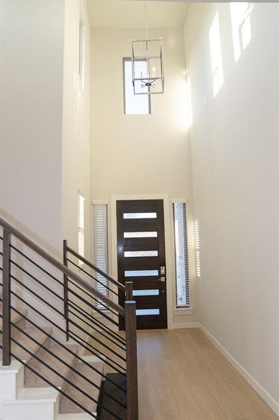 Two-story entryway featuring wood-finish flooring, a contemporary dark wood entry door with frosted glass panels, and a modern rectangular chandelier Two-story entryway featuring wood-finish flooring, a contemporary dark wood entry door with frosted glass panels, and a modern rectangular chandelier