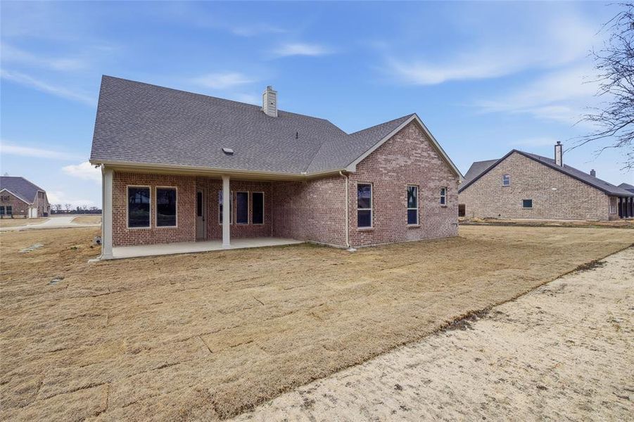 Rear view of house featuring a shingled roof, a patio area, brick siding, and a chimney