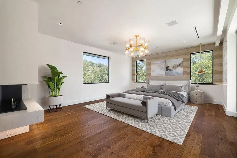 Bedroom with dark wood finished floors, a fireplace with raised hearth, and multiple windows