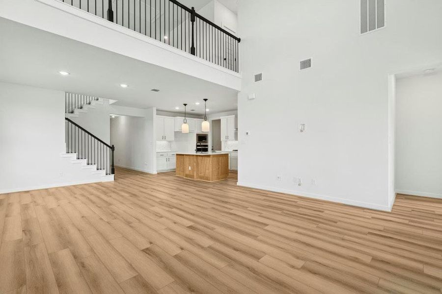 Unfurnished living room with light wood-style flooring, a towering ceiling, and stairway