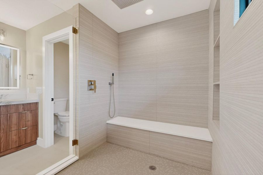 A spacious, naturally illuminated shower with elegant tiled walls and a convenient integrated bench.