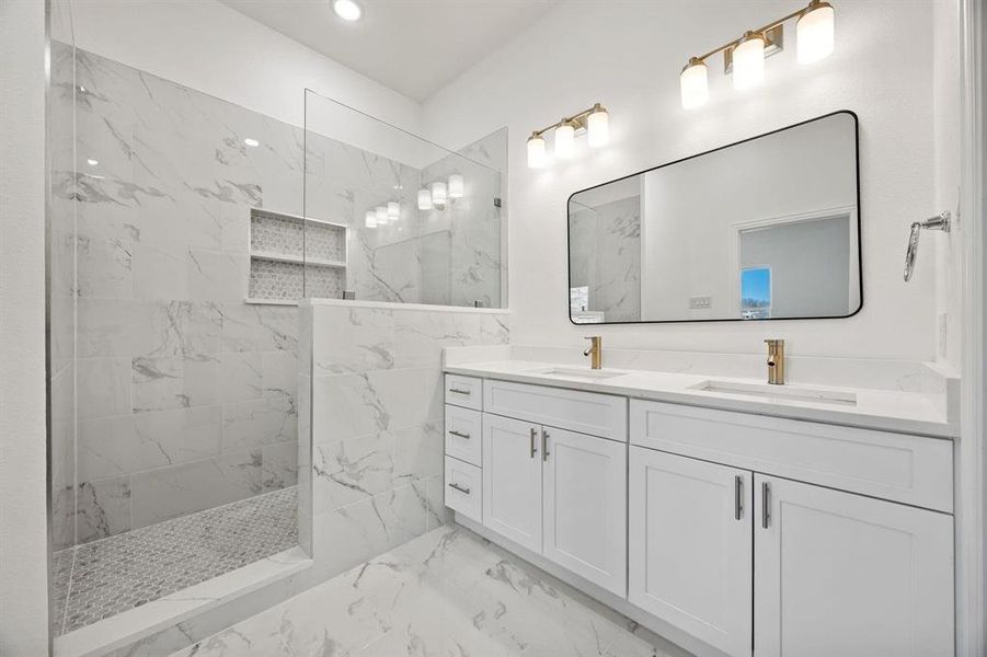 Spacious bathroom featuring a frameless glass shower enclosure, built-in shower niche, dual vanity with undermount sinks, and gold-finish fixtures Spacious bathroom featuring a frameless glass shower enclosure, built-in shower niche, dual vanity with undermount sinks, and gold-finish fixtures