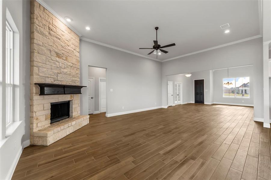 Unfurnished living room with plenty of natural light, ceiling fan, a stone fireplace, and ornamental molding