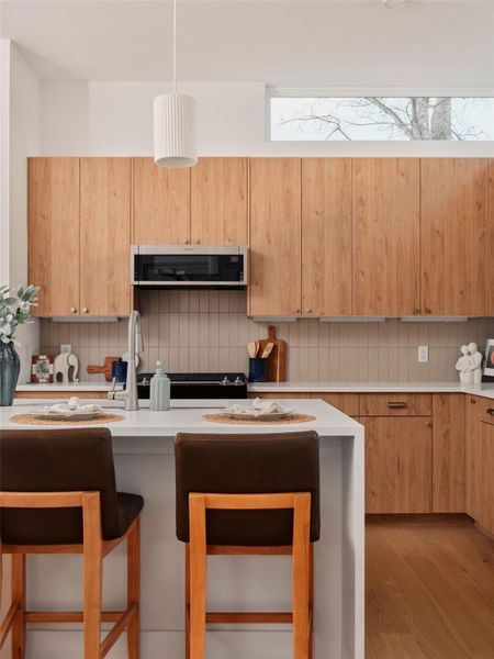 Kitchen with a kitchen breakfast bar, tasteful backsplash, light wood finish cabinetry, a center island with sink, and modern cabinets
