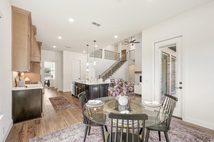 Open-concept dining area with glass table, dark chairs, and kitchen island visible with staircase in background