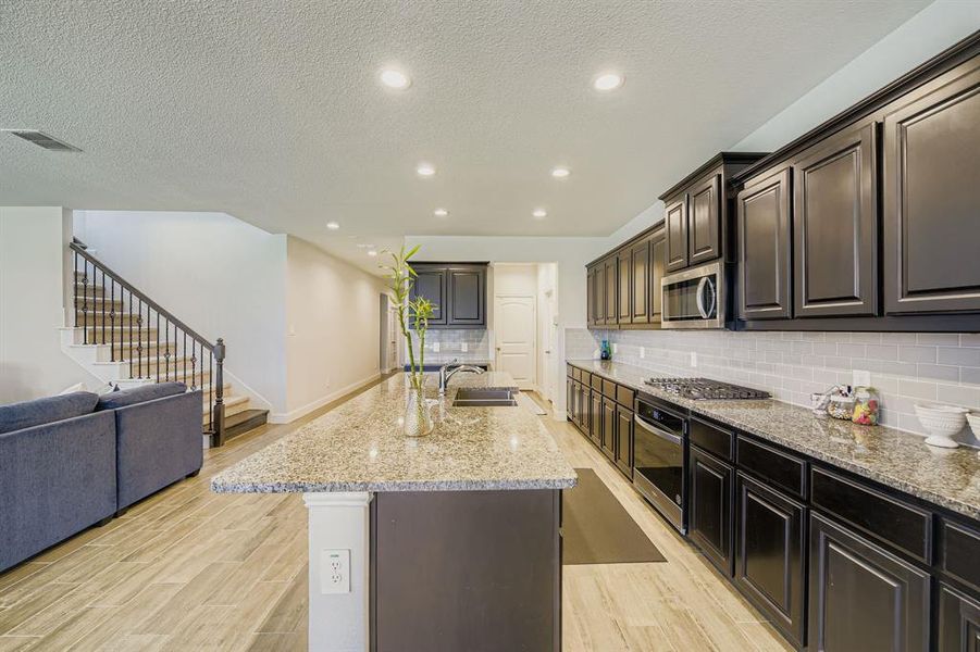 Kitchen featuring a kitchen island with sink, open floor plan, recessed lighting, a textured ceiling, and light wood-style floors Kitchen featuring a kitchen island with sink, open floor plan, recessed lighting, a textured ceiling, and light wood-style floors