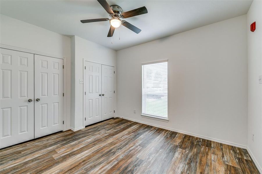 Unfurnished bedroom featuring ceiling fan, dark hardwood / wood-style floors, and multiple closets