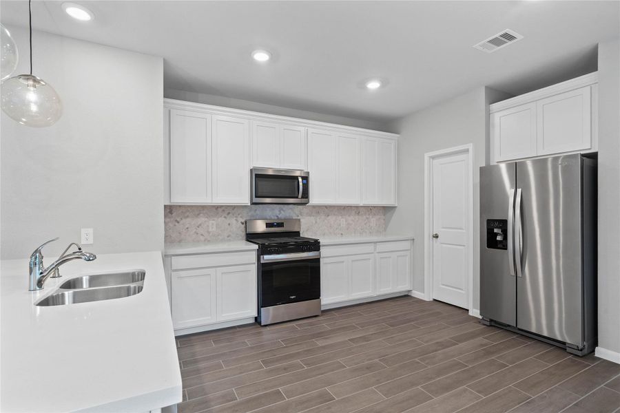 Discover this chef-ready kitchen featuring sleek, white shaker-style cabinetry, frost white quartz countertops, and a full suite of stainless steel appliances, including an over-the-range microwave and a side-by-side refrigerator.