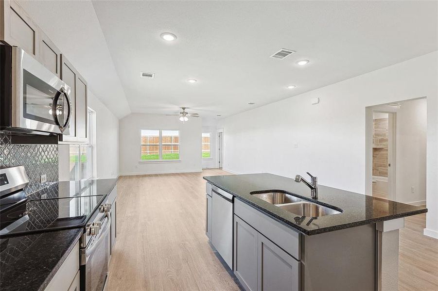 Kitchen featuring dark stone countertops, light wood-type flooring, appliances with stainless steel finishes, sink, and decorative backsplash