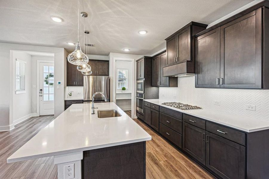 Kitchen with a kitchen island with sink, stainless steel appliances, and decorative pendant lights