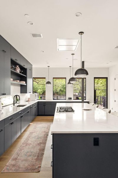 A well-lit culinary space features a spacious island with a gas cooktop, sleek cabinetry, and ample natural illumination from large windows. A well-lit culinary space features a spacious island with a gas cooktop, sleek cabinetry, and ample natural illumination from large windows.