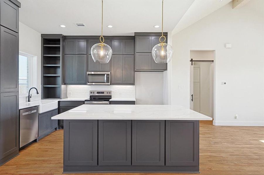 Kitchen featuring a kitchen island, a barn door, hanging light fixtures, stainless steel appliances, and vaulted ceiling