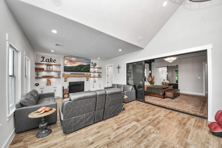 Spacious living area with vaulted ceilings, featuring a cozy fireplace, sleek built-in shelving, and an open view into a stylish adjoining room.