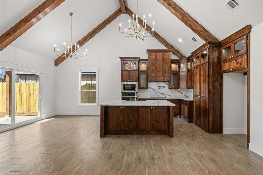 Kitchen featuring glass fronted cabinets, hanging lights, dark wood finish cabinets, an island with sink, and dark wood-type flooring
