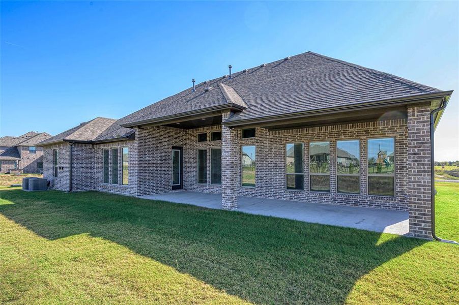 Back of property featuring a patio area, brick siding, roof with shingles, and a lawn