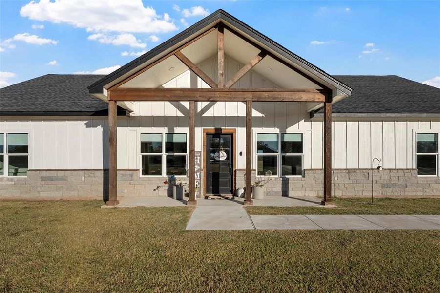 Back of property with a shingled roof, board and batten siding, a porch, and a yard