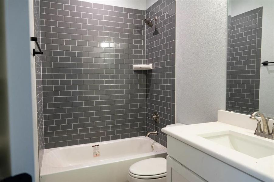 Full bathroom with vanity, tiled shower / bath combo, and toilet