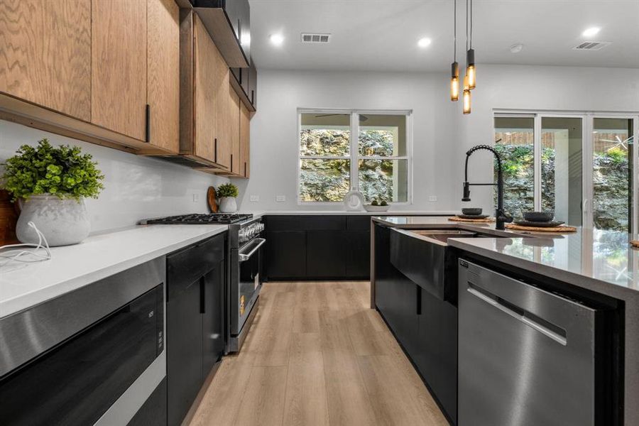 Kitchen featuring stainless steel appliances, dark cabinets, pendant lighting, modern cabinets, and light wood-style flooring