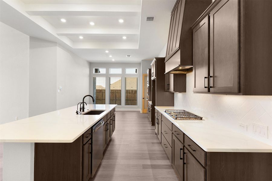 Kitchen with dark brown cabinets, a large island with sink, recessed lighting, backsplash, and a tray ceiling