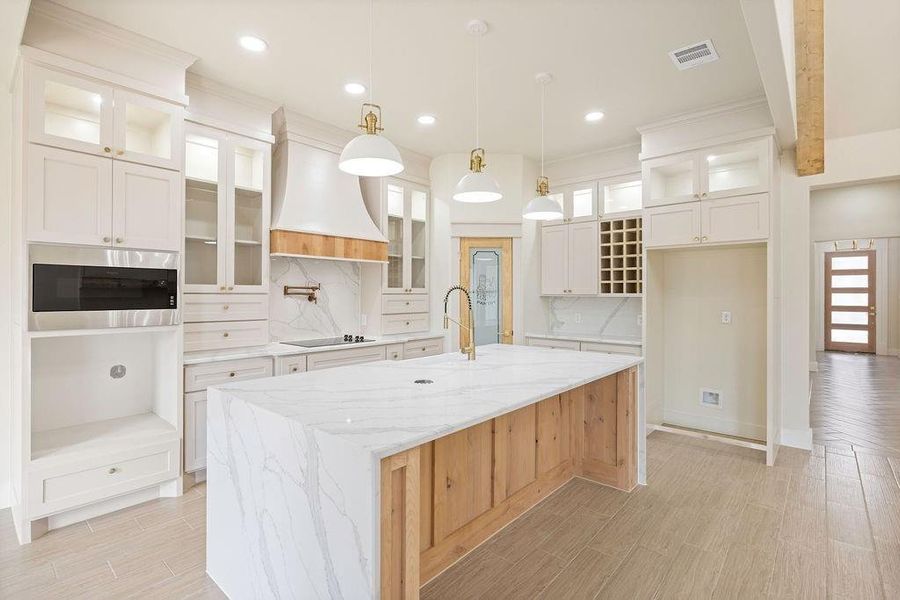 Kitchen with black electric stovetop, custom exhaust hood, visible vents, a sink, and an island with sink