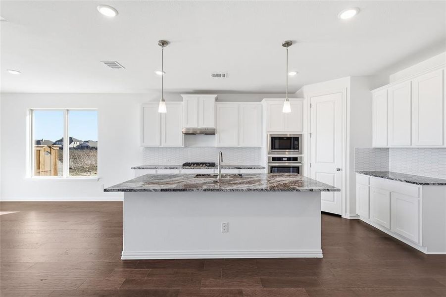 Kitchen featuring a large island with stone countertops, white cabinetry, built-in stainless steel appliances, a white tile backsplash, and wood-finish flooring
