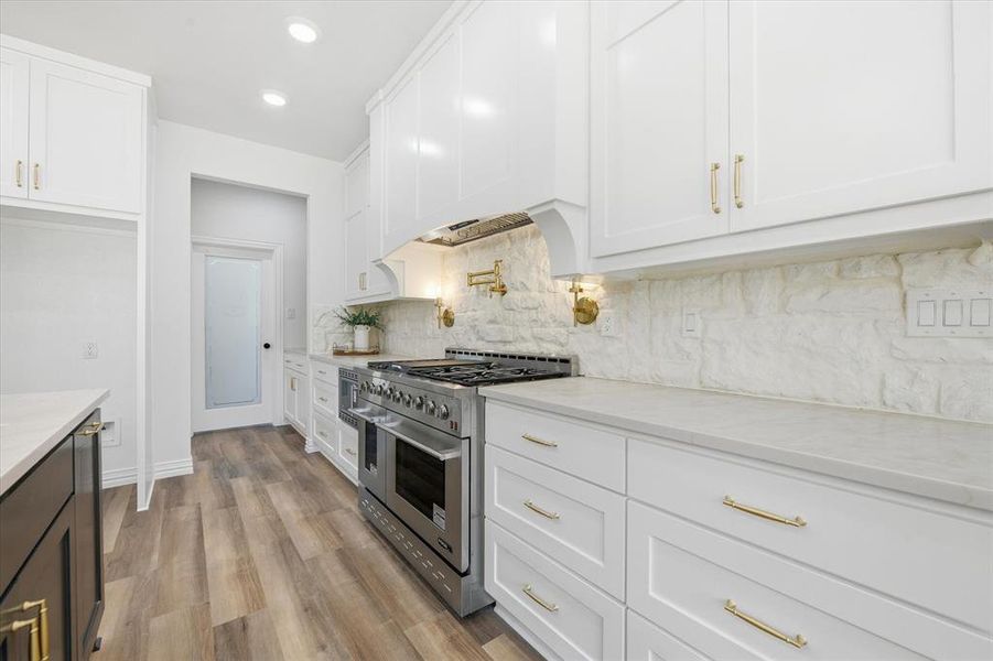 Dual tone kitchen with range with two ovens, light stone countertops, light wood finished floors, recessed lighting, and two tone color scheme