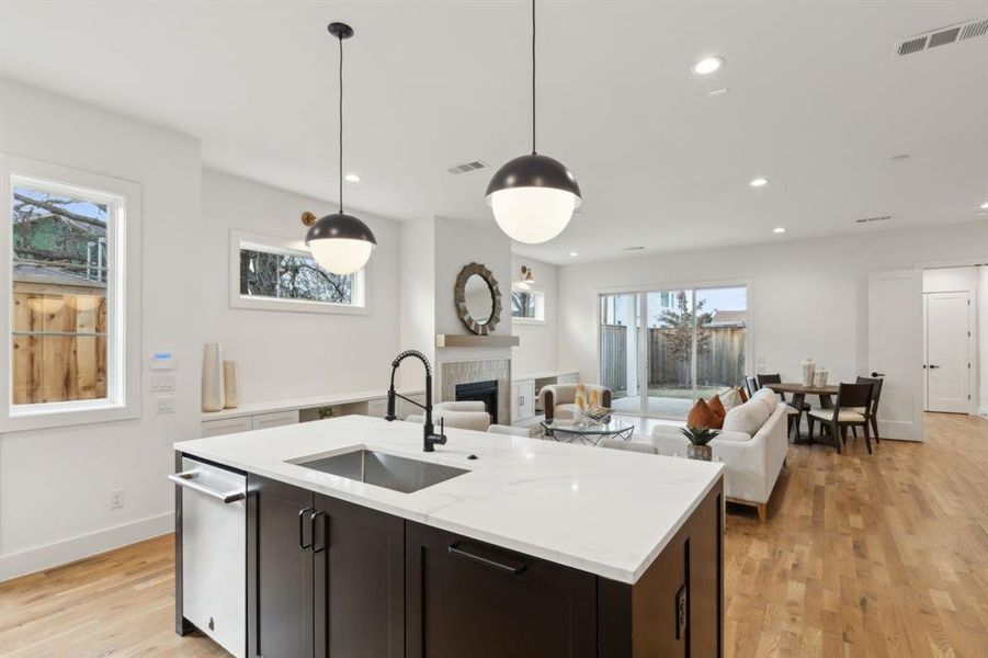 Kitchen featuring a tile fireplace, light hardwood / wood-style floors, light stone counters, sink, and decorative light fixtures