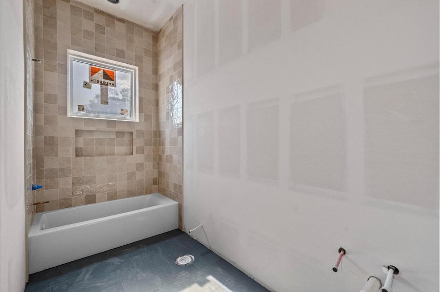Secondary bathroom designed with dark tile flooring,warm-toned shower tile and white oak cabinetry with a mix of black and brass hardware.