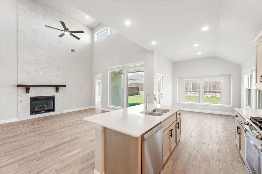 Open-concept kitchen with island sink, vaulted ceiling, and marble tile fireplace in adjoining living area