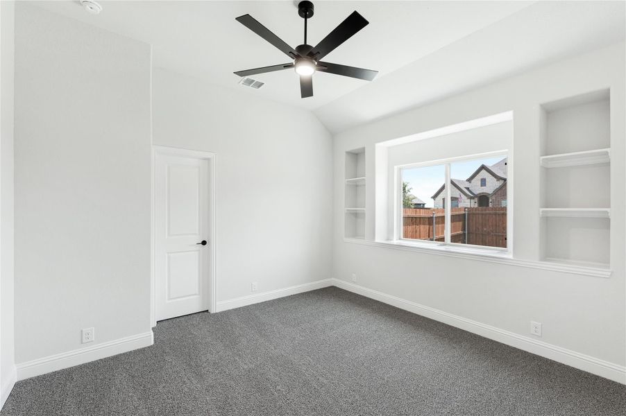Empty bedroom with vaulted ceiling, black ceiling fan, built-in shelves, and gray carpet