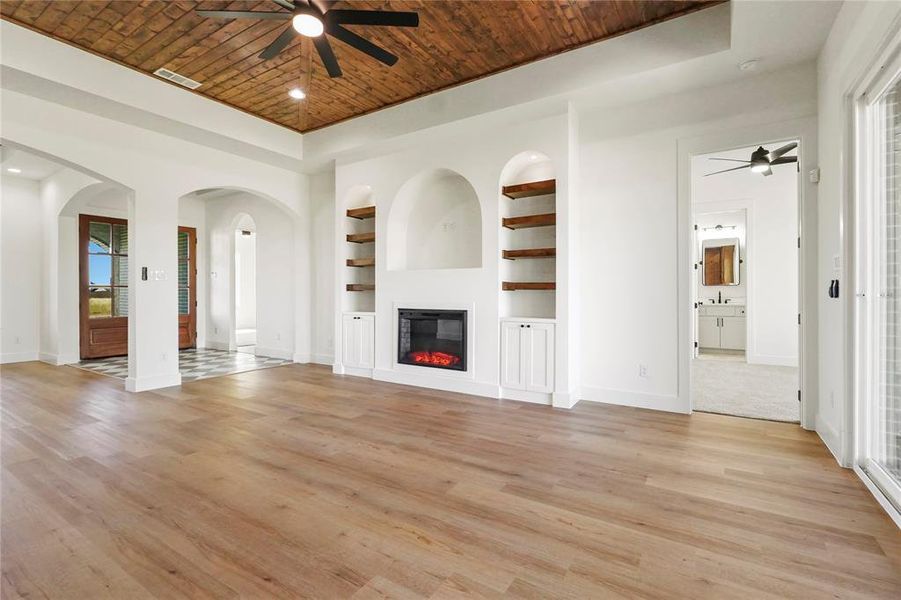 Unfurnished living room with a ceiling fan, built in shelves, light wood-type flooring, a glass covered fireplace, and wood ceiling Unfurnished living room with a ceiling fan, built in shelves, light wood-type flooring, a glass covered fireplace, and wood ceiling