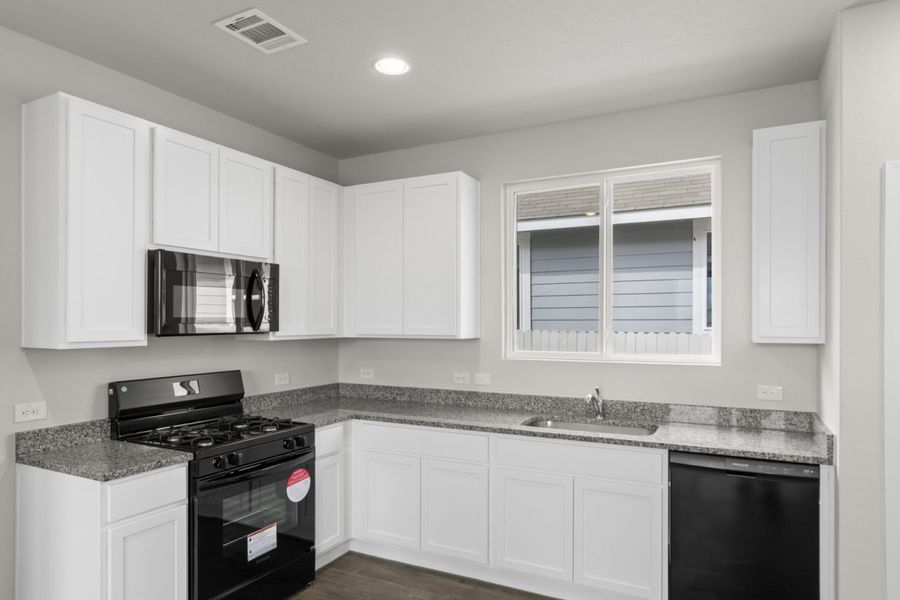 Image of a one story home kitchen with white cabinets and black appliances with a window over the sink