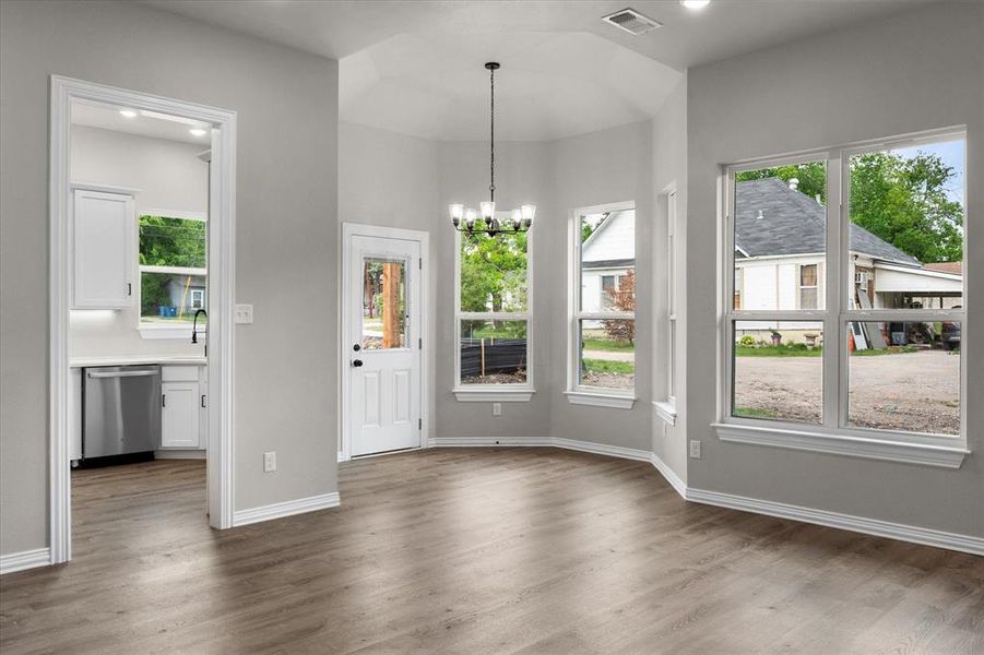 Bright dining area featuring wood-finish flooring, a modern chandelier, and multiple large windows with white trim