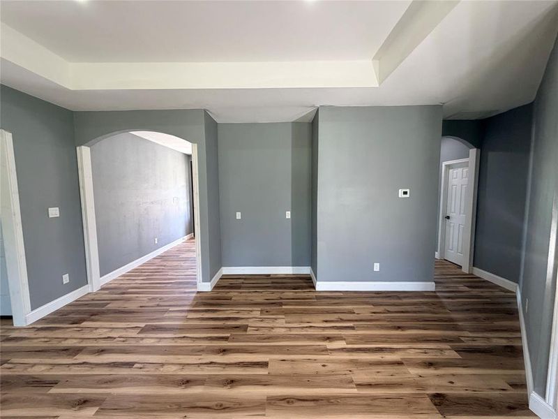 Expansive living area featuring tray ceilings, wood-finish flooring, and arched doorways with white trim