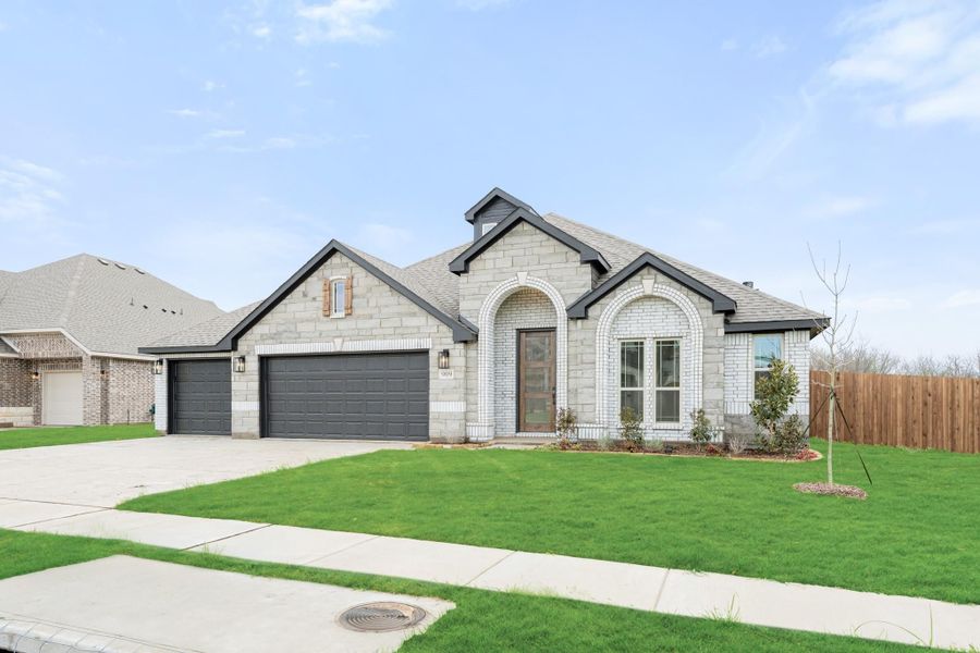 Single-story home with stone and brick exterior, arched entry, two-car garage, and green front lawn