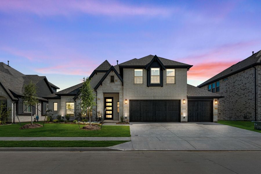 Two-story home with light stone exterior, three-car garage, and manicured front lawn at dusk Two-story home with light stone exterior, three-car garage, and manicured front lawn at dusk