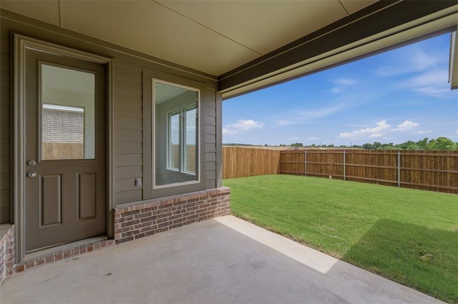 Covered concrete patio opening to an expansive fenced yard featuring a level lawn and wood privacy fencing