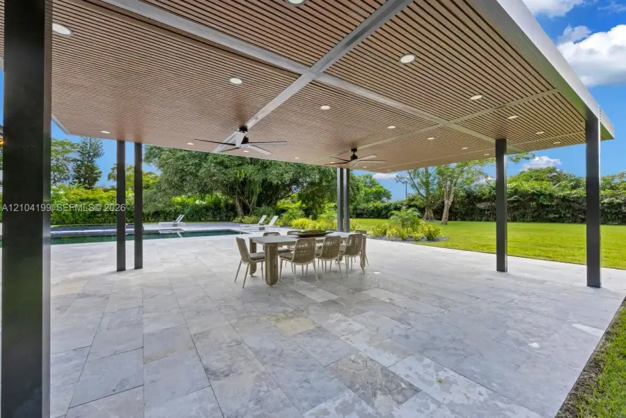 Covered outdoor patio featuring a slatted wood-finish ceiling, recessed lighting, ceiling fans, stone paver flooring, and a swimming pool