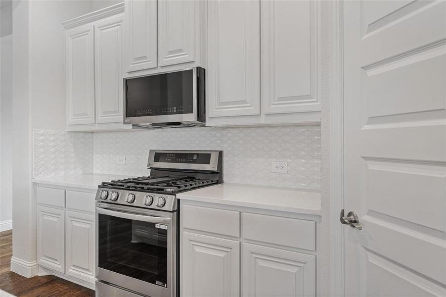 Kitchen featuring stainless steel appliances, white cabinets, light stone countertops, and decorative backsplash